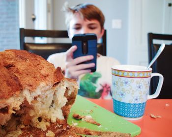 Close-up of food against boy using phone at home