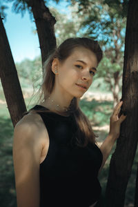 Portrait of young woman looking away while standing against trees