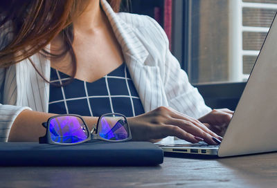 Midsection of woman using phone while sitting on table