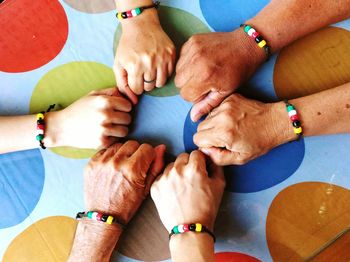 Cropped hands of friends wearing colorful bracelet on table