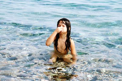 High angle view of topless girl holding nose in water at beach