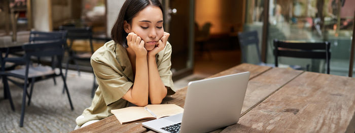 Young woman using laptop while sitting on table