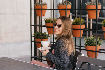 Stylish young woman in sunglasses drinks cappuccino coffee in a summer cafe, looking away. person