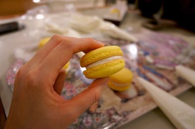 Cropped image of woman holding yellow macaroon at bakery