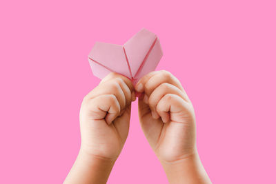 Close-up of hand holding paper against pink background