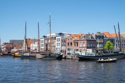 Sailboats moored on canal by buildings against clear sky