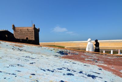 Rear view of man and woman walking on building against sky