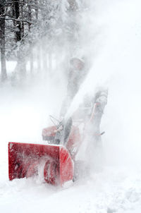 Male worker is covered in snow, as he walks behind a snow blower