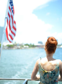 Rear view of woman looking at sea while traveling on boat with flag