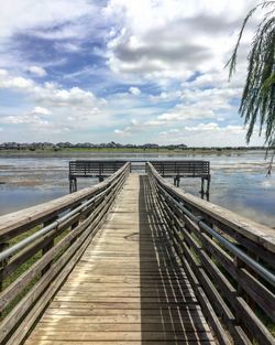 View of wooden bridge over calm lake against sky