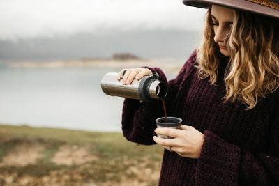 Woman wearing hat standing at riverbank during winter