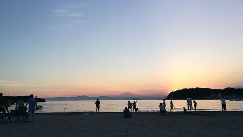 Silhouette people on beach against sky during sunset