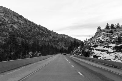 Empty road along trees and mountains against sky