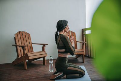 Woman sitting on chair by table against wall