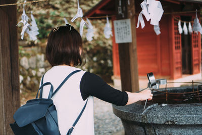 Rear view of woman holding umbrella against building