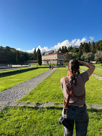 Rear view of man photographing while standing on field against clear blue sky