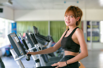 Portrait of smiling young woman on exercise bike at gym