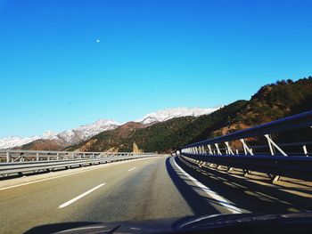 Road seen through car windshield against clear blue sky