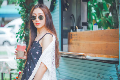 Portrait of young woman holding drink standing outdoors