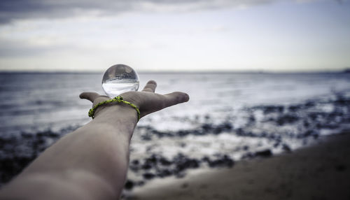 Cropped hand holding crystal ball at beach