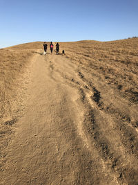 People walking on sand dune against clear sky