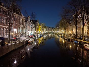 Boats moored in canal amidst buildings in city at night