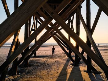 Rear view of man standing on pier at beach against sky