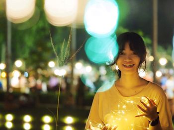 Portrait of smiling woman holding illuminated lights at night