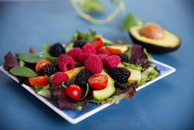 Salad with red berries, cherry tomatoes and avocado, on a blue table.