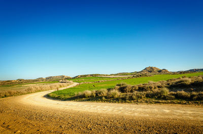 Scenic view of road amidst field against clear blue sky