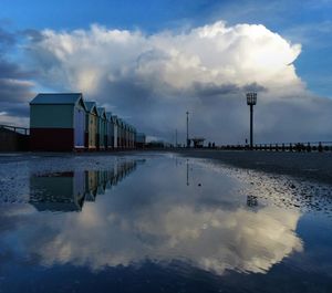 Sky reflecting on puddle by beach huts