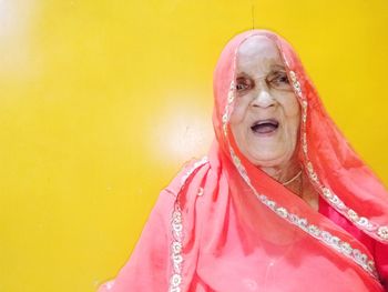 Portrait of senior woman in pink sari against yellow wall at home