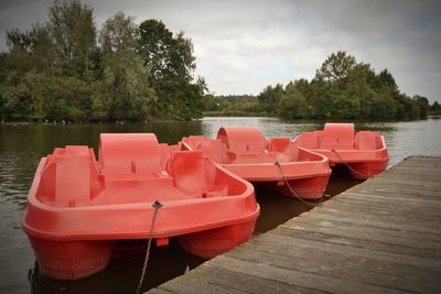 Red boats moored in lake against sky