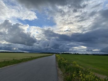 Empty road amidst field against sky