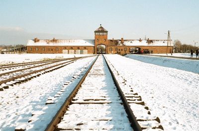 Railroad tracks by building against sky during winter