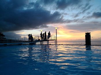 Silhouette people standing by sea against sky during sunset