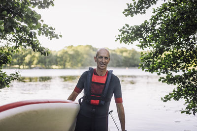 Mature man wearing wetsuit and life jacket while holding paddleboard