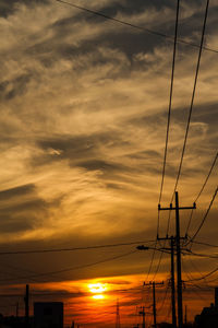 Low angle view of silhouette electricity pylon against dramatic sky