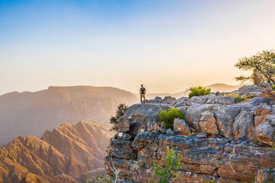 Distant view of hiker standing on mountain against sky during sunset