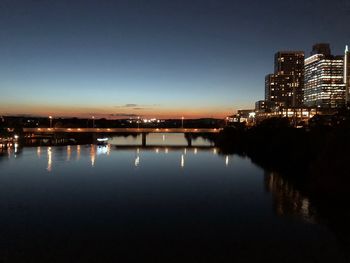 River by illuminated buildings against clear sky at night