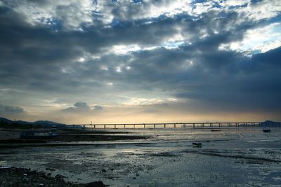 View of bridge over calm sea against cloudy sky