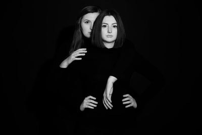 Portrait of young woman standing against black background