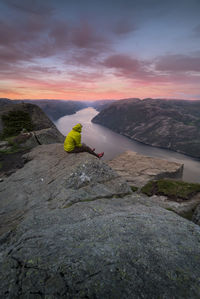High angle view of woman sitting on cliff by river during sunset