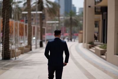 Rear view of man walking on footpath against buildings