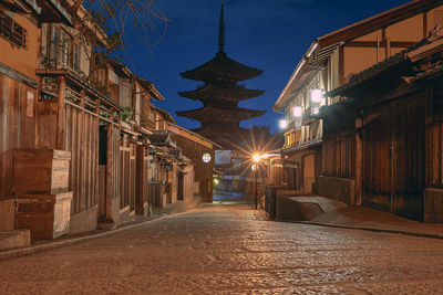 Illuminated street amidst buildings against sky at night