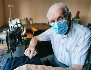 Portrait of senior man wearing mask sewing at home