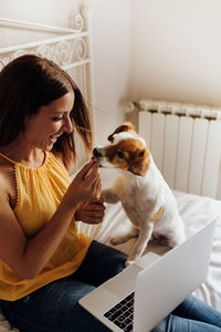 Woman playing with dog while sitting with laptop at home