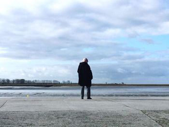 Rear view of man standing on footpath against cloudy sky