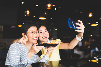 Smiling mother and daughter taking selfie with food in restaurant
