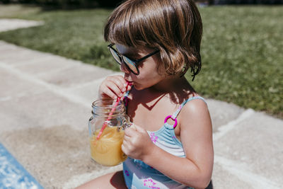 Close-up of girl drinking juice at poolside during sunny day